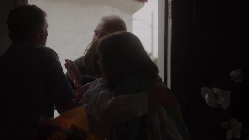A group embraces in a doorway during an emotional reunion their faces mostly in shadow against the bright outside light