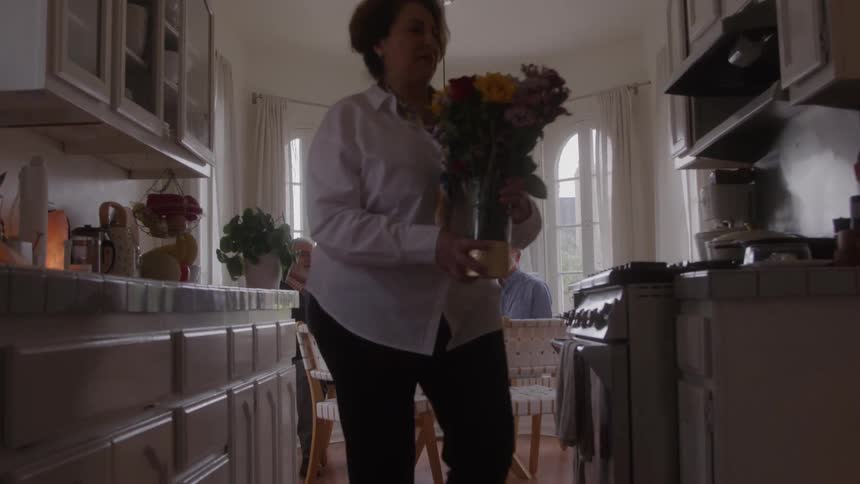 Two women carrying flowers and food and two elderly men sitting in the background
