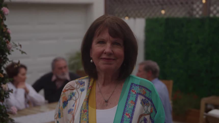 Woman smiles gently during an outdoor gathering with friends in the background