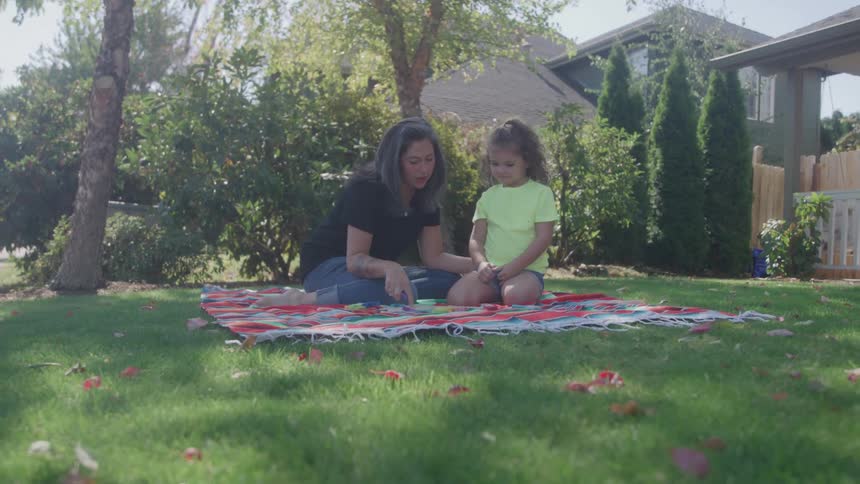 Woman talks with a child while sitting on a picnic blanket in the yard