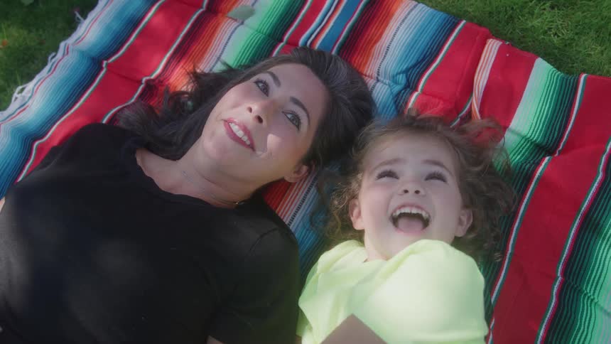 Mother and daughter lay together on a blanket on the grass