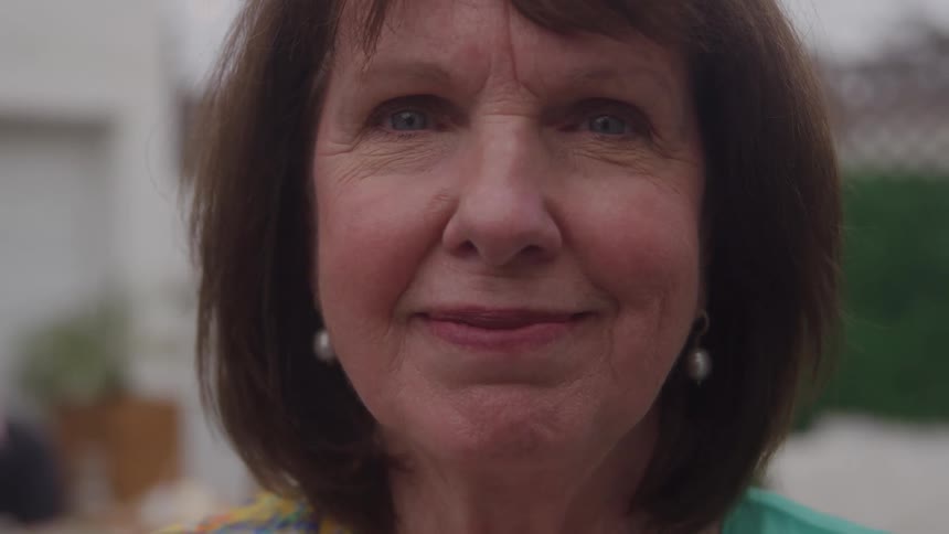 Older woman with brown hair smiles slightly in an outdoor setting