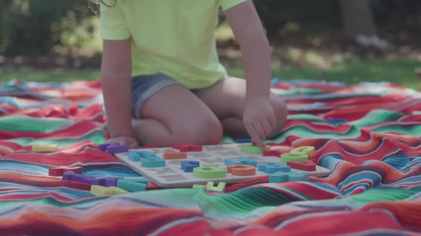 Child plays with colorful alphabet pieces on a striped blanket