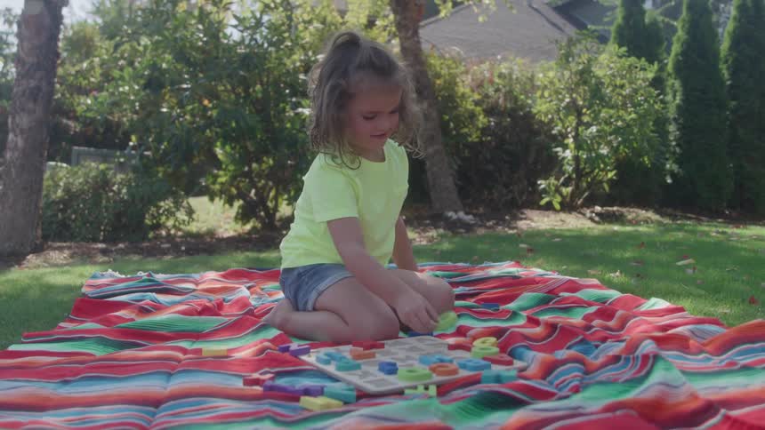 Little girl in green shirt lying on suspended swing holds the edges with her hands in a treelined outdoor area