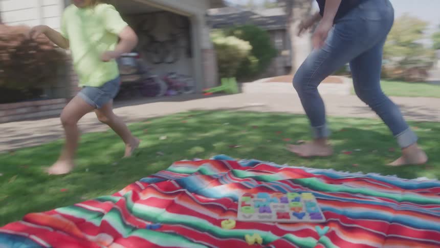 Woman and child run barefoot on the grass near a colorful blanket