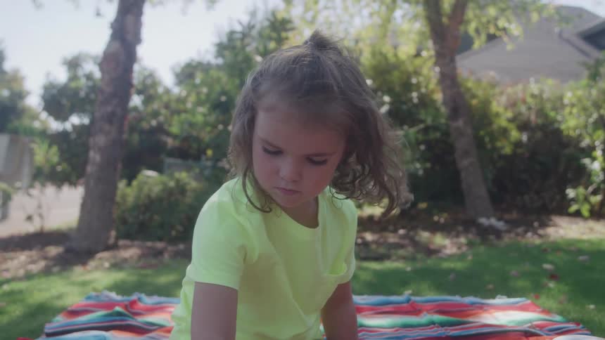Little girl sitting on a colorful blanket plays on the grass