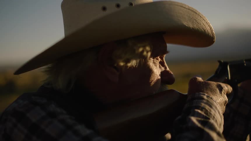 An old man adjust his hat before raising his rifle to his shoulder