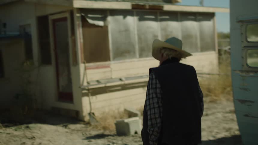 An old man carries a gun as he walks toward a ramshackle house