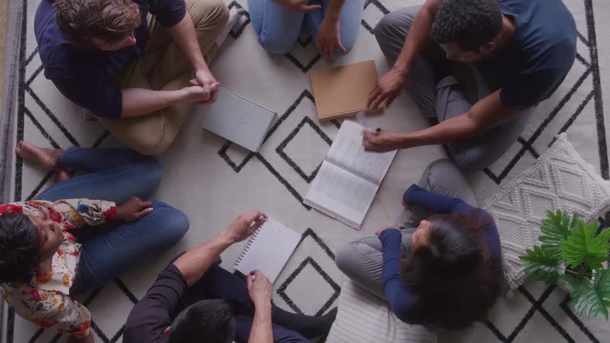 Group of people sitting in a circle on the floor with open books and notebooks
