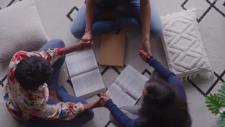 Three people sitting in a circle holding hands with open books in front of them