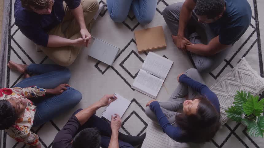Friends sit in a circle on a patterned rug with notebooks open chatting and planning together