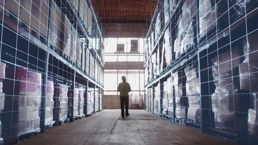 A male worker walking through a loaded storage warehouse during daytime