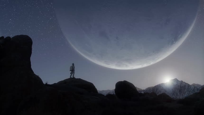 Backpacker climbs onto a rock formation then looks at the large moon hanging in the starry night sky