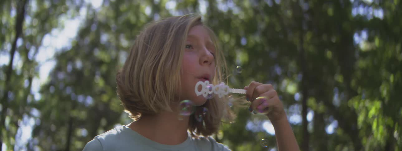 The girl is blowing bubbles outside