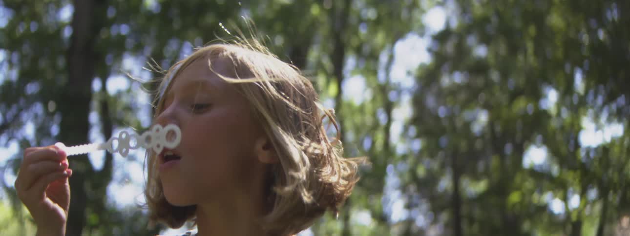Close up of a girl blowing bubbles with a bubble wand while playing outdoors during daytime