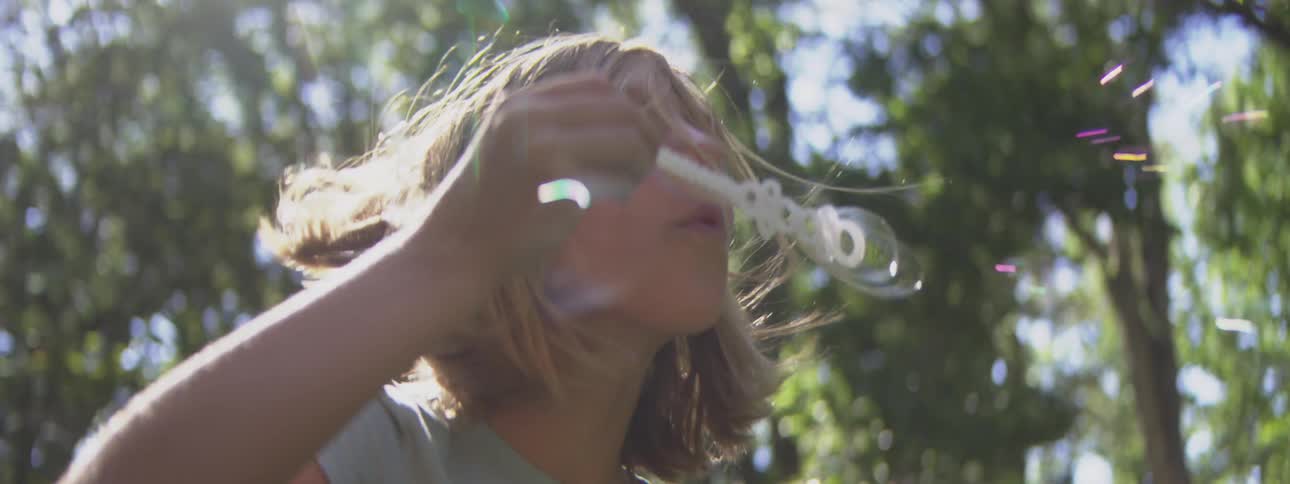 Child blowing soap bubbles under sunlight among the trees