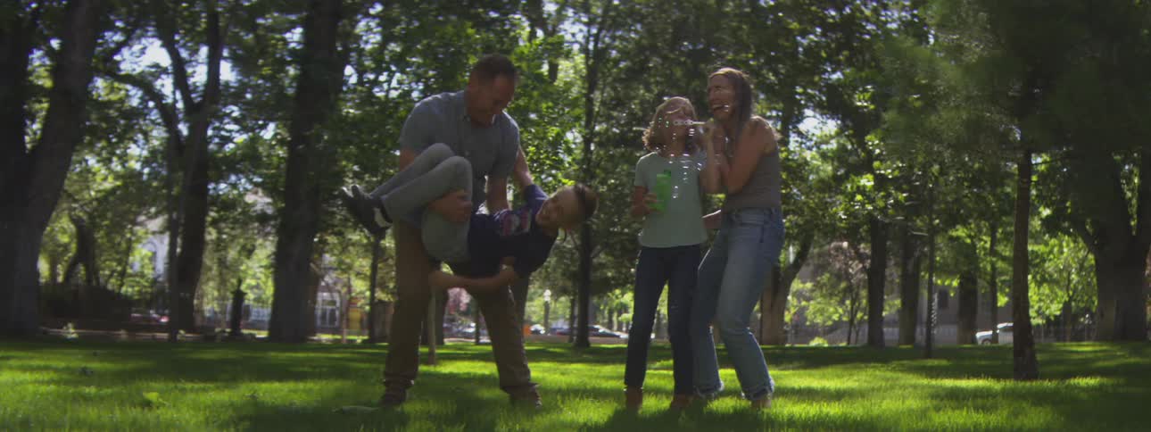 A family of fourmother father and two sonsenjoys a sunny midday at the park one son gleefully blows bubbles from a device sharing smiles and playful moments in the open air