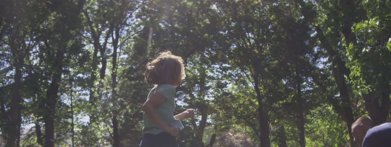 Children running and playing in a sunny park surrounded by trees