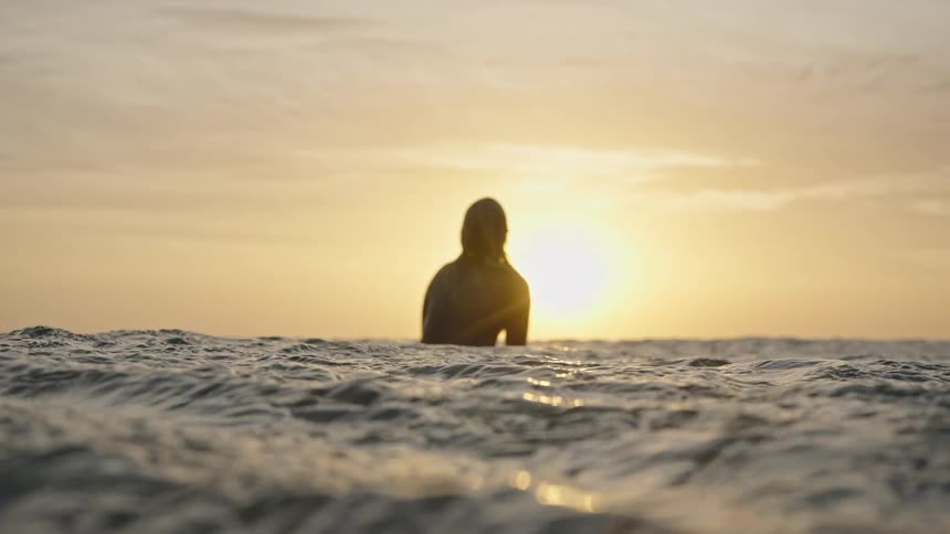 The woman lays on her surfboard while watching the sunrise