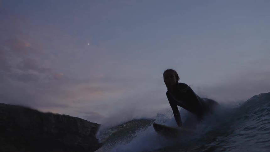 A surfer in a dark wetsuit rides a large wave at the coast during sunset