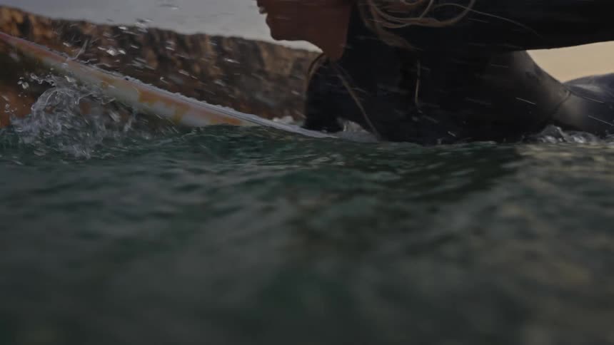 Surfer in a wetsuit paddling on the board at sunset