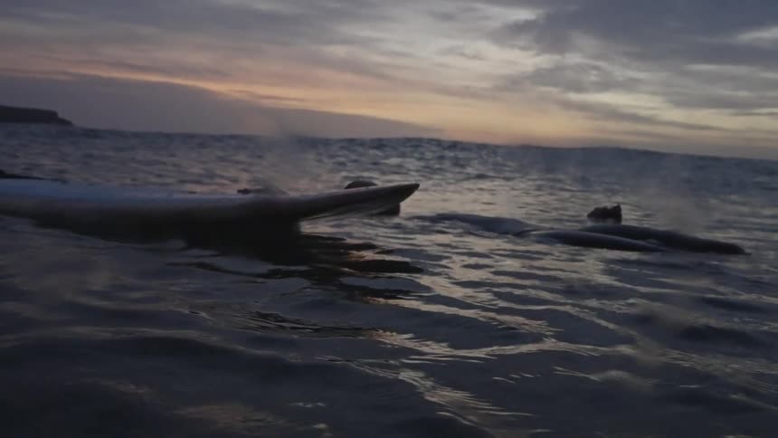 The person floats in the water by their surfboard