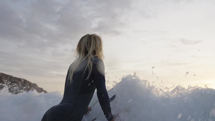 Blonde female surfer wearing a wetsuit struggles against an incoming wave near dawn