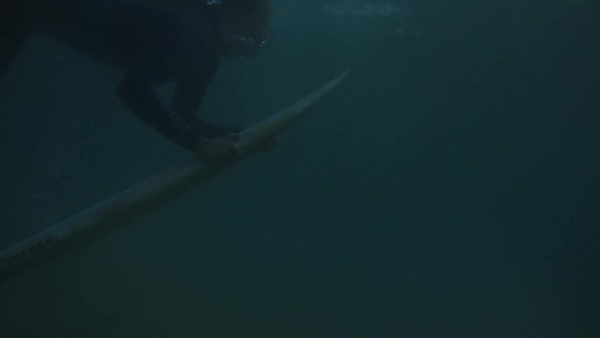 A young woman rides her surfboard in the ocean at sunset holding it steady as she glides across the glowing water