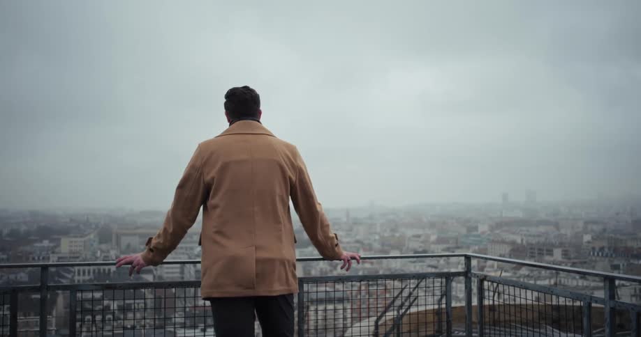The man looks out over the city from a balcony