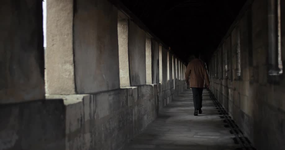 Man wearing a jacket walking on a corridor made of stone indoors during day time