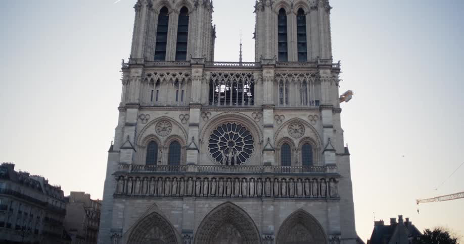 The video is a wide frontal shot of the notre dame cathedral in paris before its major restoration several people are visible in the square walking towards the three distinct arched doorways that dominate the lower facade of the building