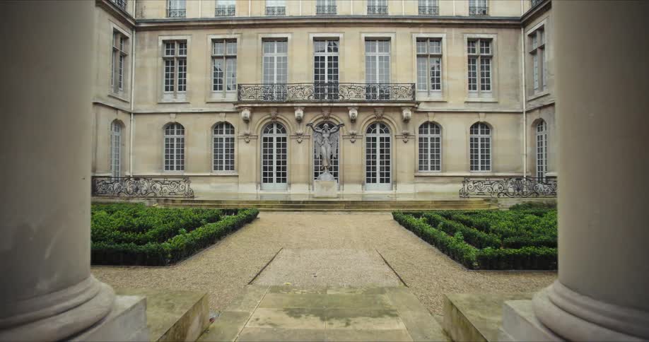 Framed between two large pillars a magnificent historic building stands at the end of a formal courtyard
