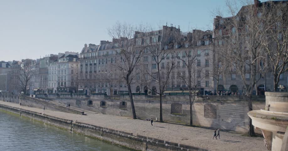 A calm riverside promenade with classic european buildings under a clear blue sky