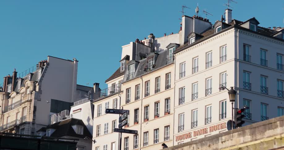 A row of pale parisian buildings with mansard roofs wroughtiron balconies and chimneys rises under a clear blue sky