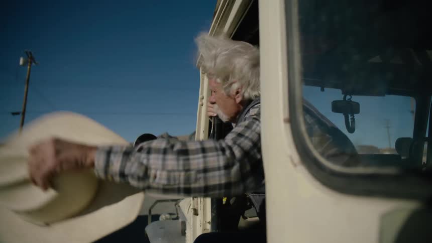 An old man leans out of his truck and tries to flag down another truck