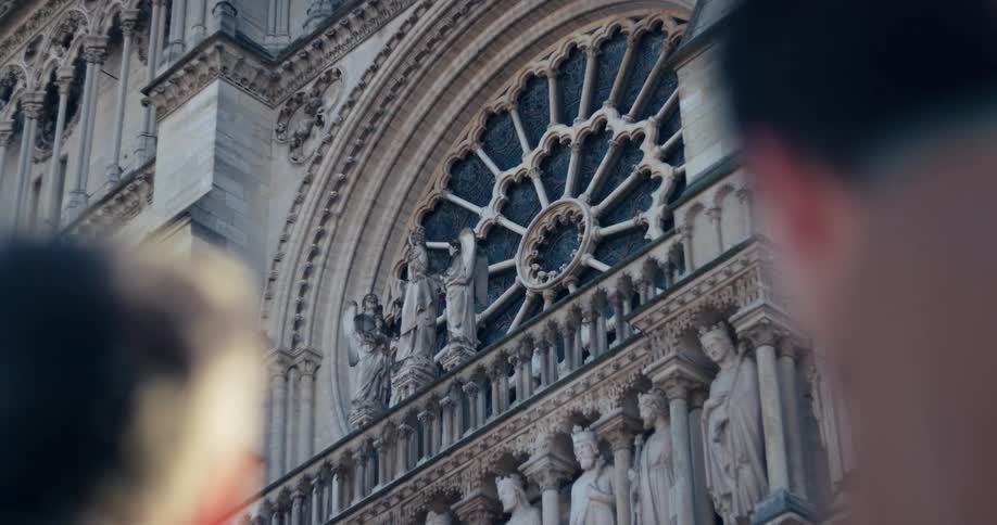 The video is a closeup of a decorative rose window on the facade of a gothic church likely notre dame cathedral in paris the architectural detail is prominent with rows of statues and carvings below the round window