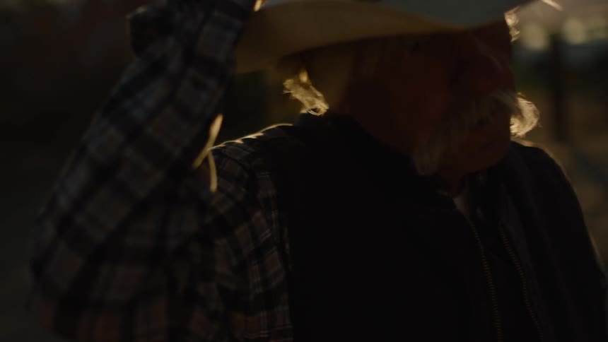 A man holds a cowboy hat on his head on a windy day