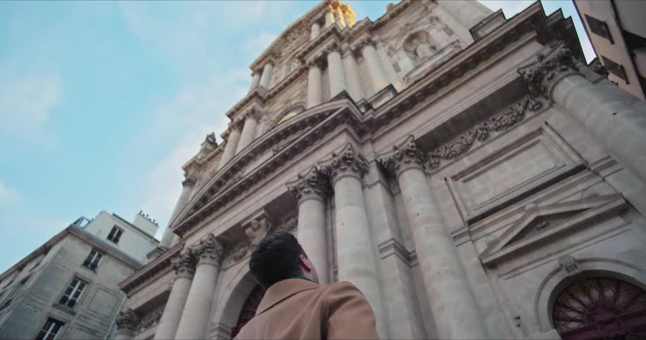 The man is looking up at the tall stone church