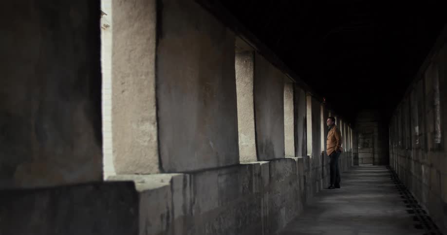 A man stands alone in a dim corridor inside an old stone building