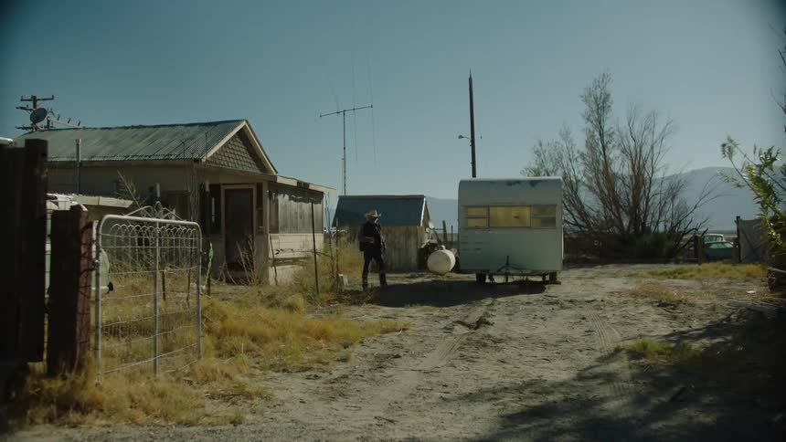 Man walks out of a house in the country towards a camper