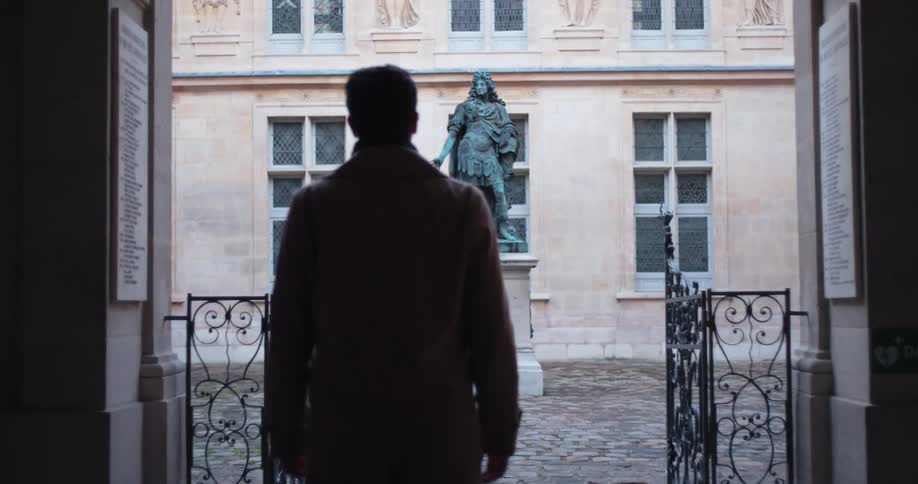 Man stands looking at the statue in a courtyard during the daytime