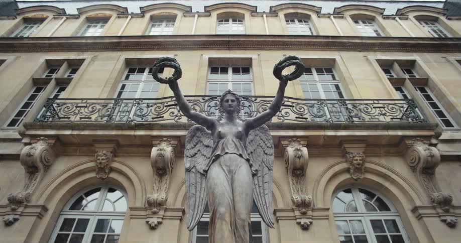Statue of an angel holding wreaths in front of an ornate stone building