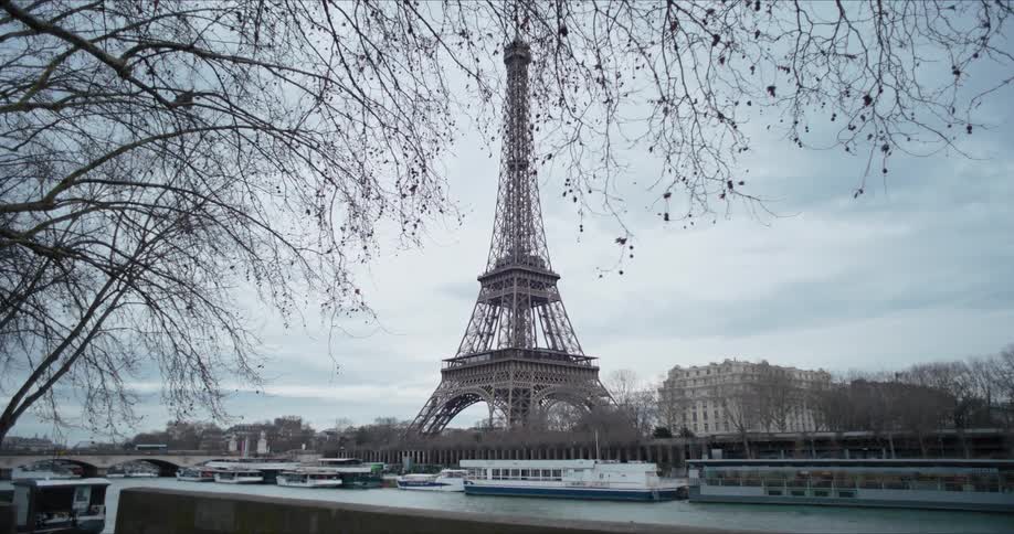 Eiffel tower seen from the riverbank under a cloudy sky