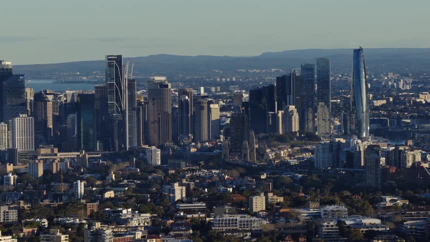 The video is an elevated wide shot providing a panoramic view of the sydney skyline on a clear day it shows a dense cluster of modern skyscrapers rising above surrounding residential buildings and parks