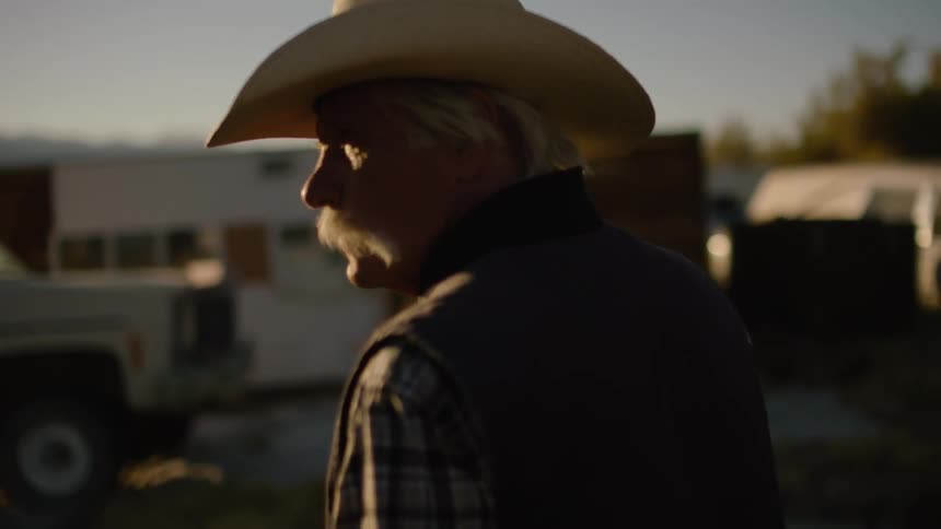 Elderly man stands outside by a camper and vehicles