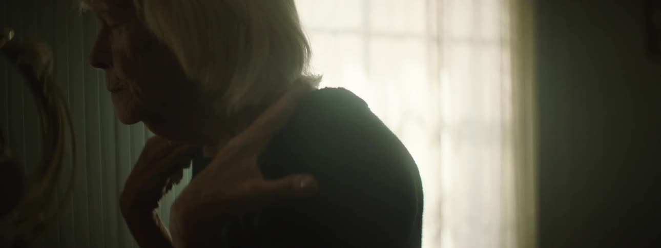 And old woman with her eyes closed reaches up and touches her shoulders