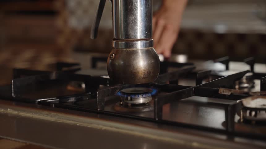 Metal coffee maker being turned on over the blue flame of the stove