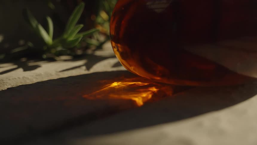 Sunlight passes through an amber bottle casting a golden reflection on the ground