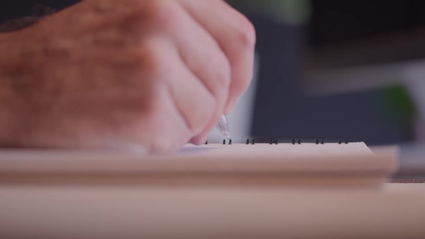 Hand writes with pen in spiral notebook over blurred surface