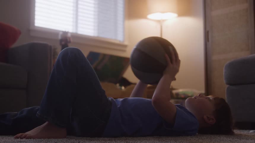 Boy lying on the floor in the living room throws and catches a basketball